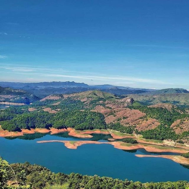 The high range seen from Calvary Mount: a blue reservoir winding between red laterite banks and wooded ridges, with mountains along the horizon.